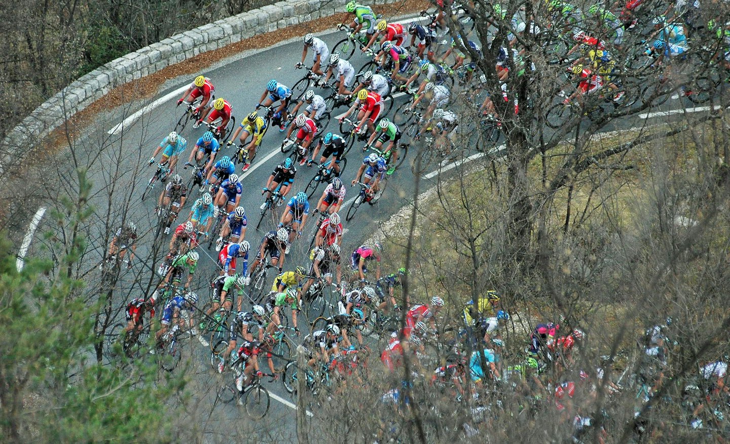 Ciclisti professionisti che gareggiano insieme in salita su una strada tortuosa.