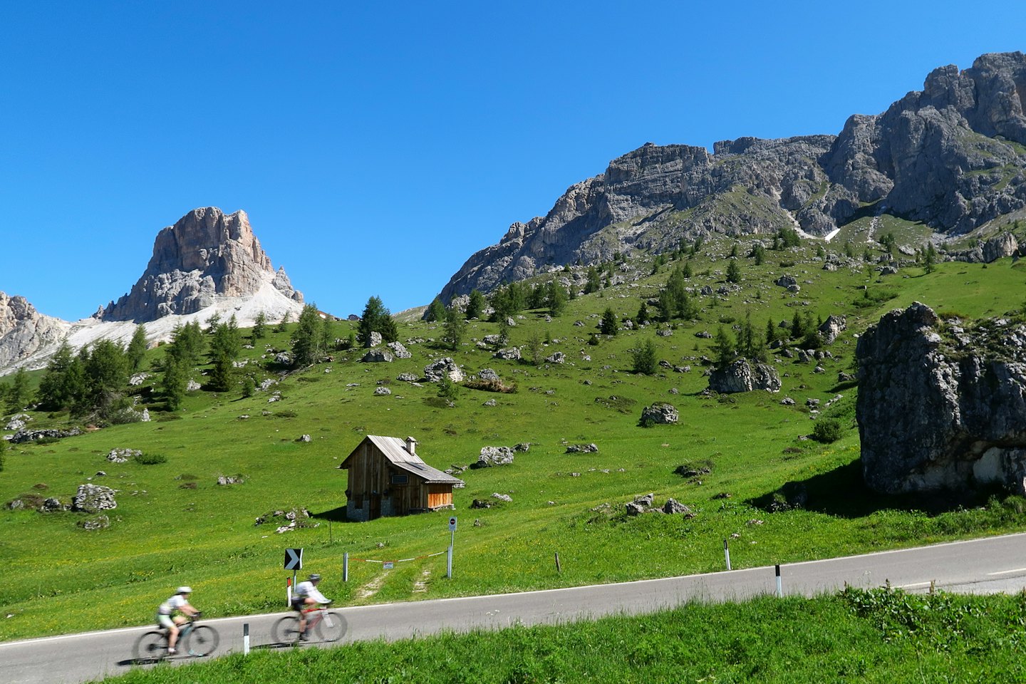 Due ciclisti pedalano su una strada asfaltata attraverso una valle montana.