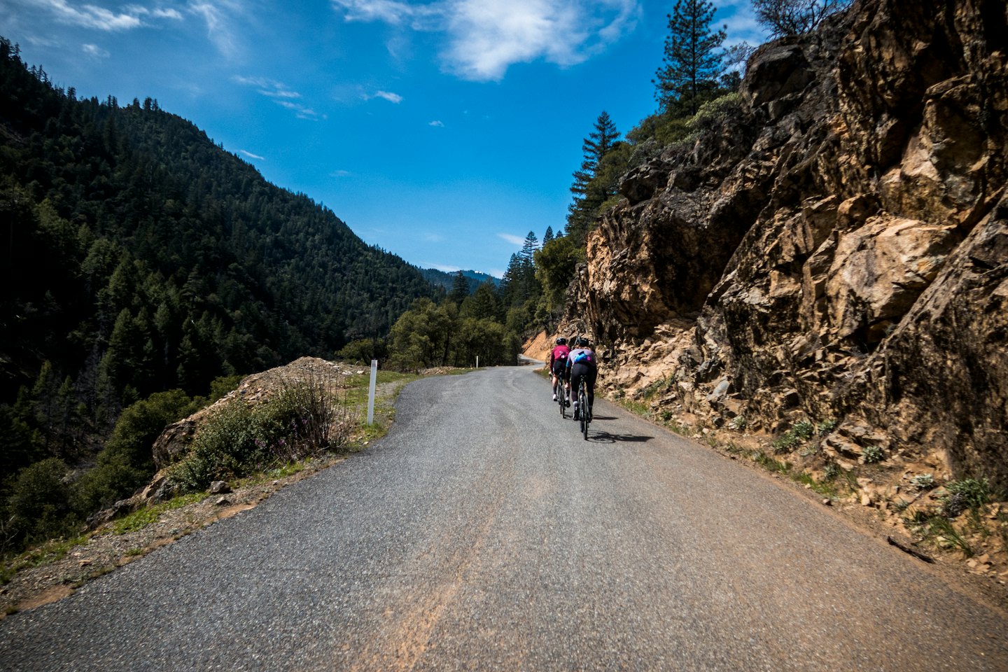 Tre ciclisti pedalano in salita su una strada di montagna tortuosa.